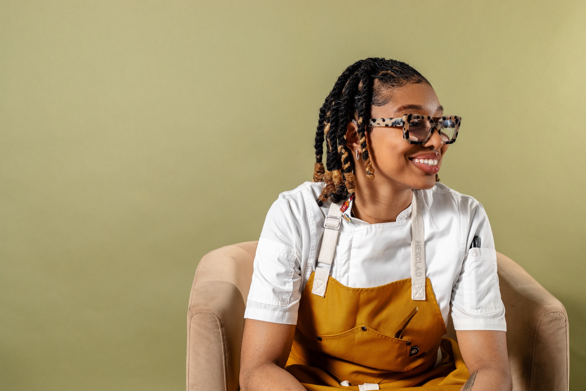 Chef Nia Spencer seated in her whites and apron, smiling