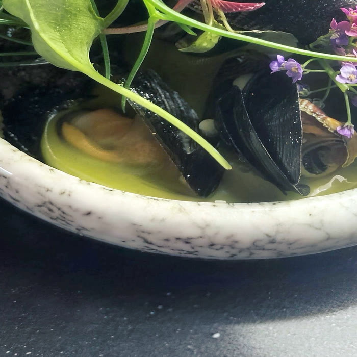 Mussels open in a green herb broth