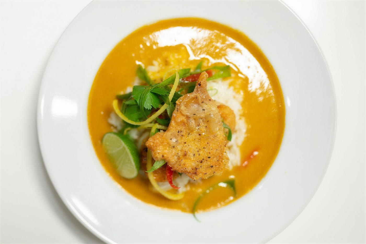 Crisp-skinned chicken over rice in a red curry with lime, chilli and herbs