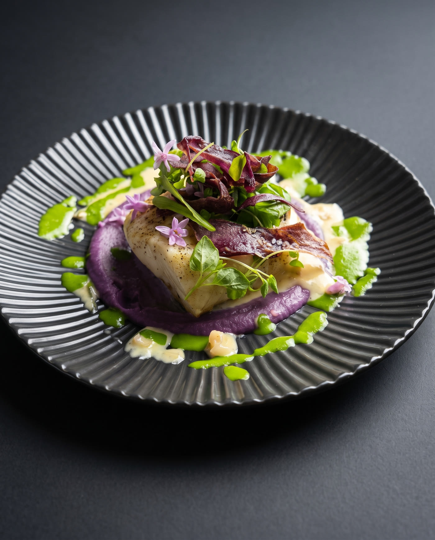 Seared halibut with beet purée, herb oil, micro herbs and edible flowers on a fluted dark plate