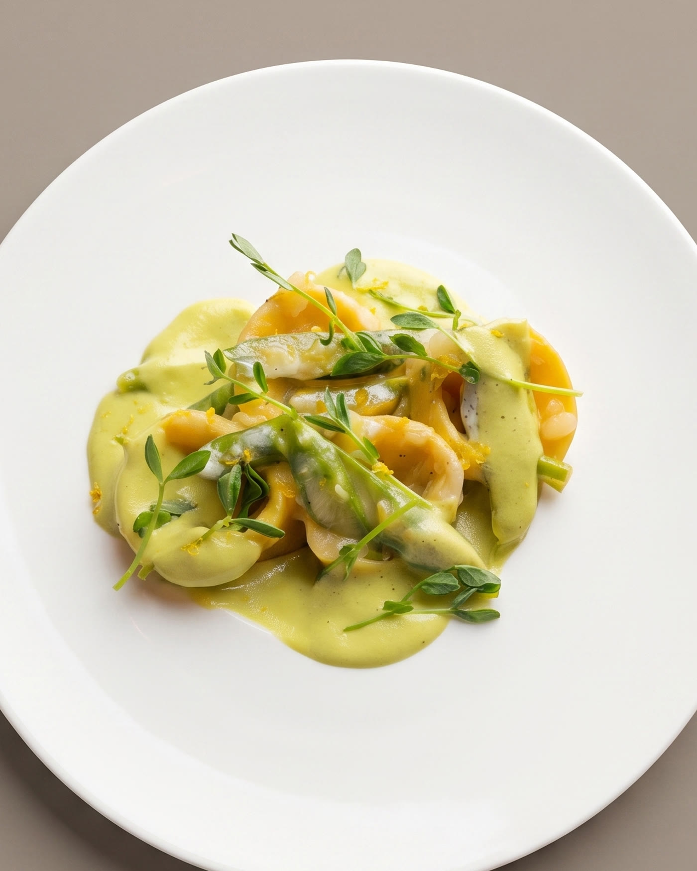 Shrimp and agnolotti in a saffron-herb sauce with pea shoots and lemon zest