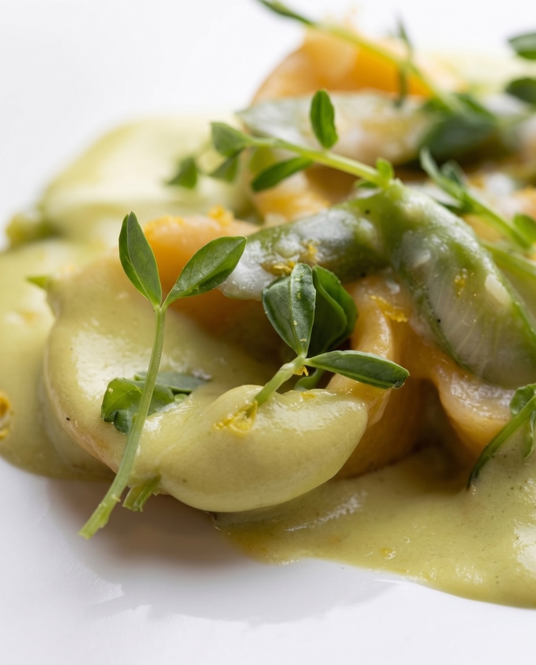 Filled pasta, shrimp and pea shoots very close, one sharp plane falling away to soft focus