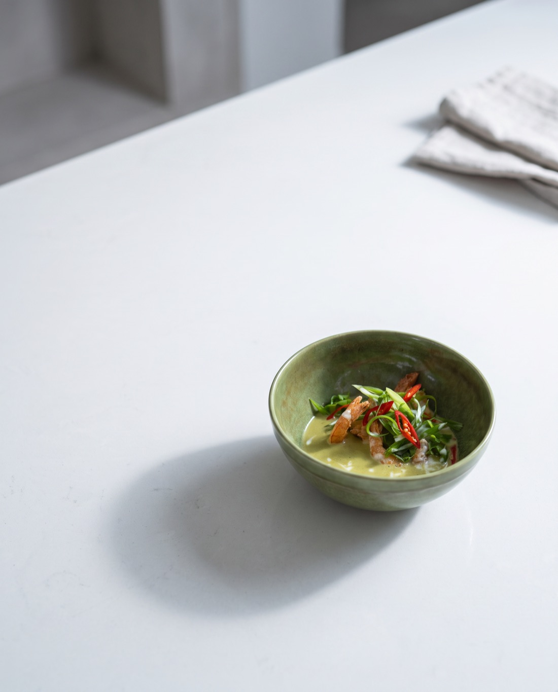 The coconut curry set small and low in a wide frame, a long soft shadow across pale stone